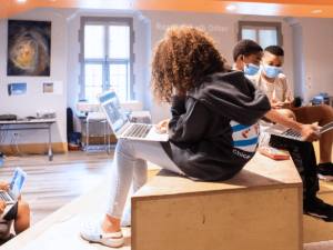 A group of students sitting on wooden structure with laptops