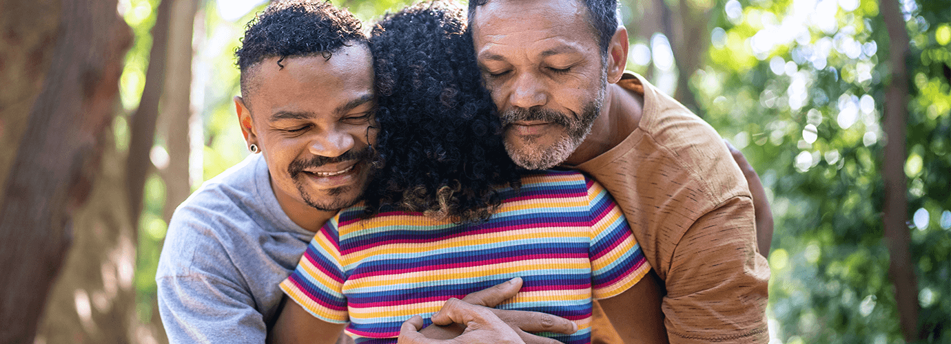 Two fathers hugging their child.
