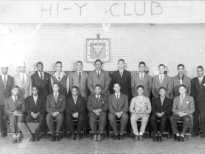 A group of Black men sitting under a sign that reads "Hi-Y Club"