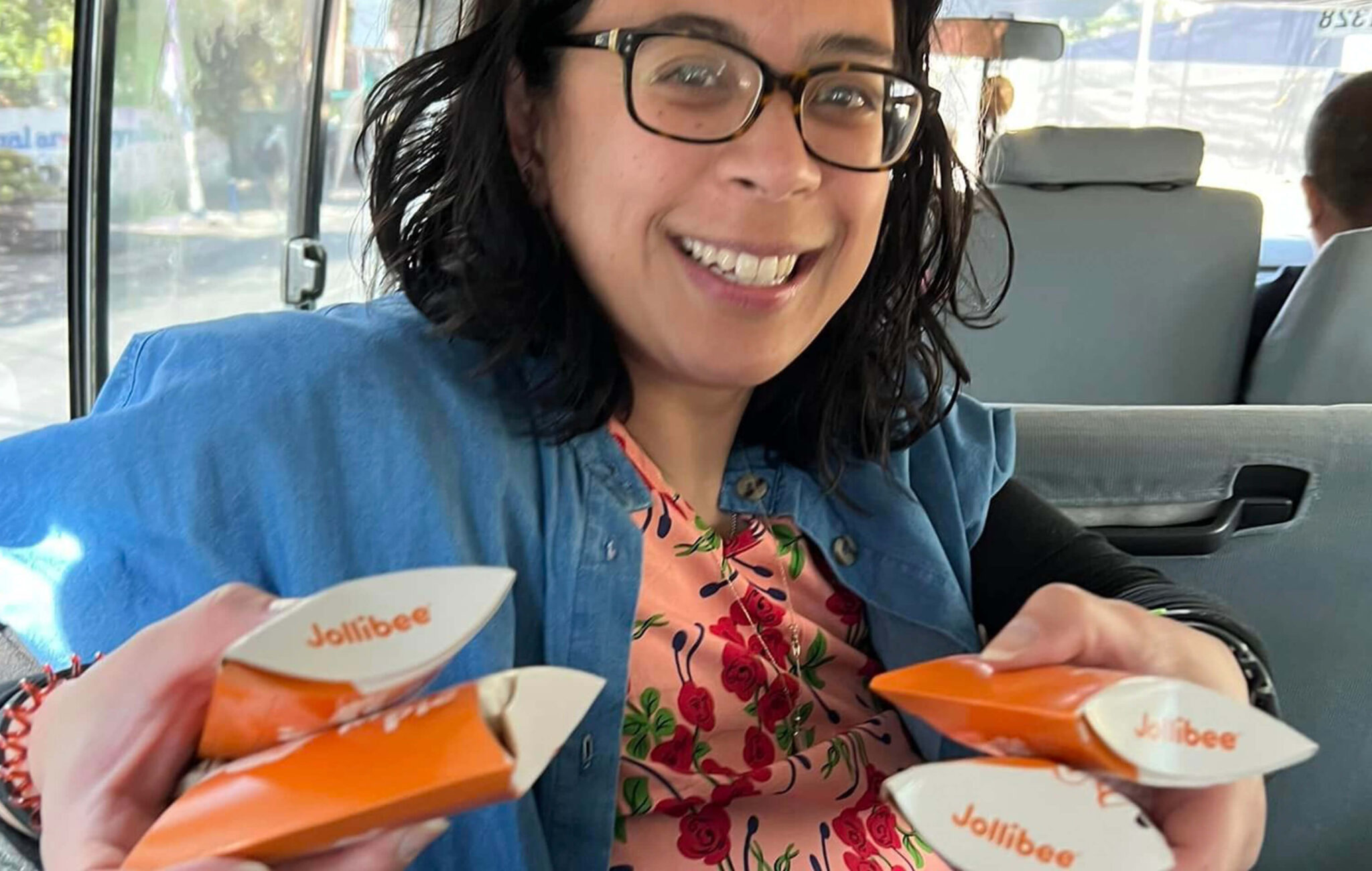 An Asian woman is smiling and sitting in a van holding four packages of handpies from a Jollibee, a Filipino fast-food restaurant.