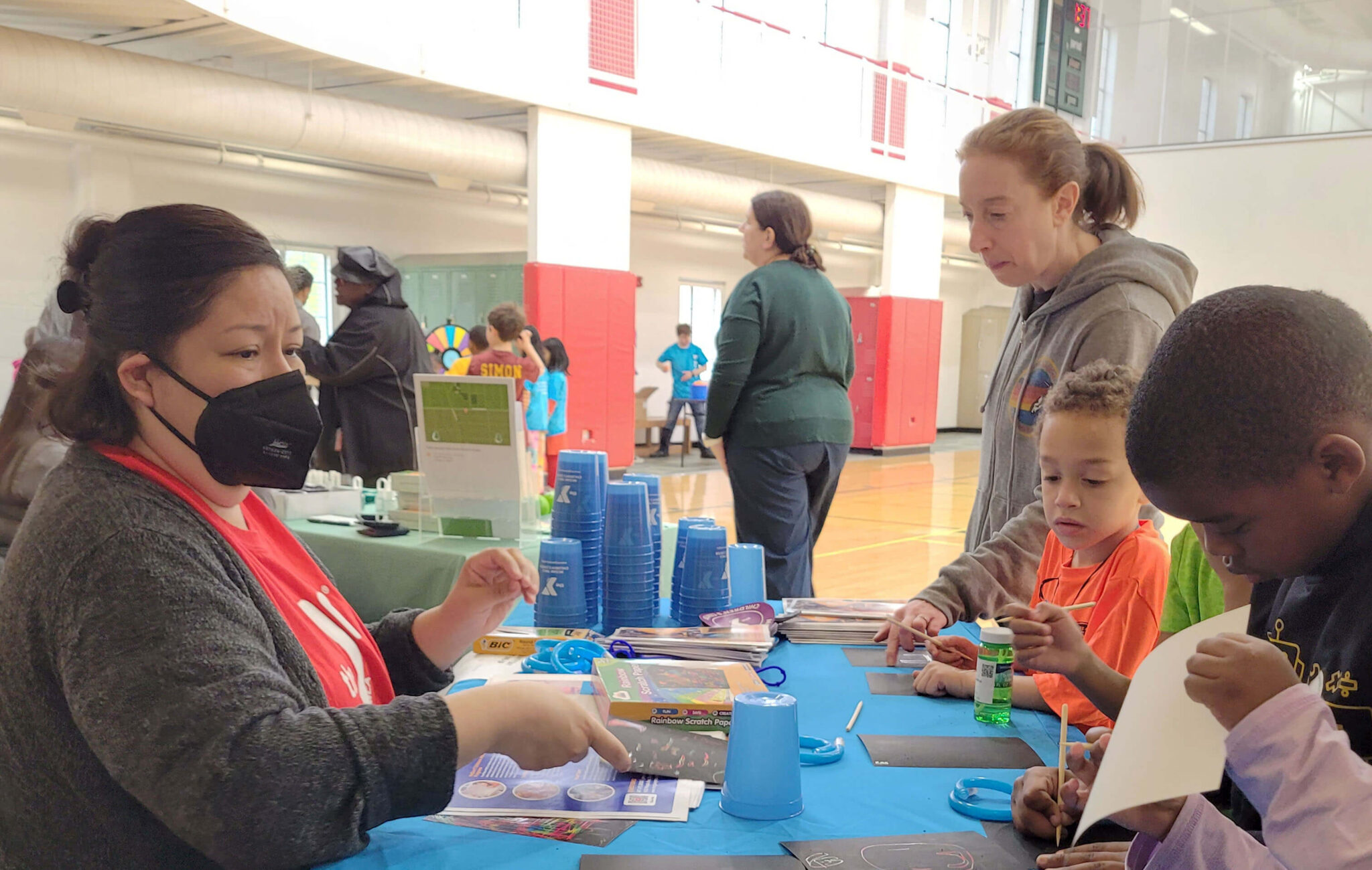 A seated woman is on side of a table and on the other side are children standing while they do scratch art.