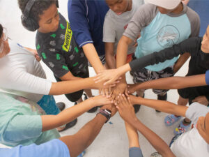 A group of Summer Day Camp kids at McGaw YMCA putting hands in a huddle.