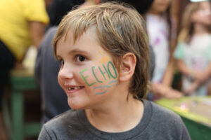 A child showing off painted words "Echo" on face at Family Camp Carnival.