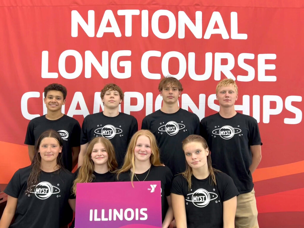 Eight swimmers from the McGaw YMCA Swim Team are pictured wearing black t-shirts. They are standing in front of a large background that reads, "National Long Course Championships." Two of the swimmers are holding a sign that says, "Illinois."