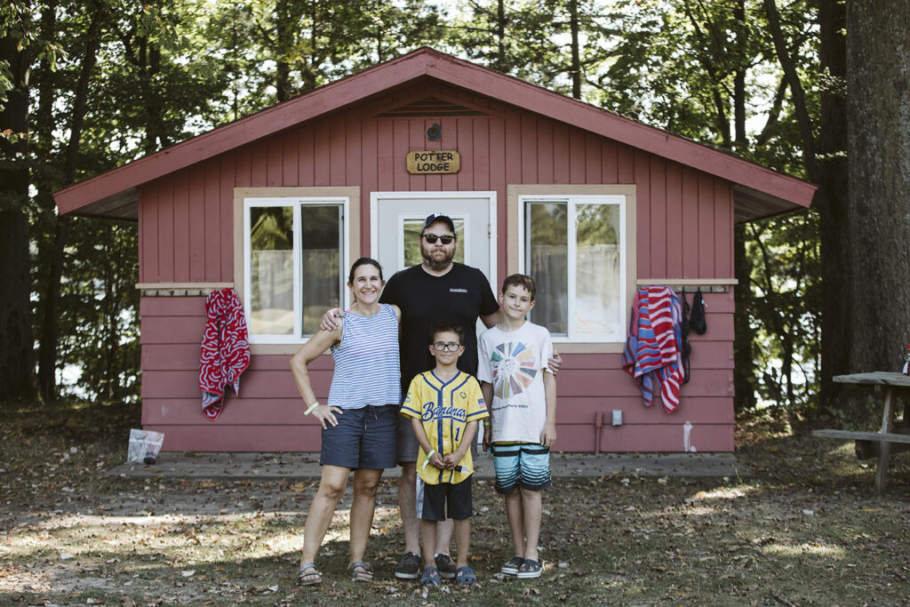 A family smiling and standing in front of a cabin.