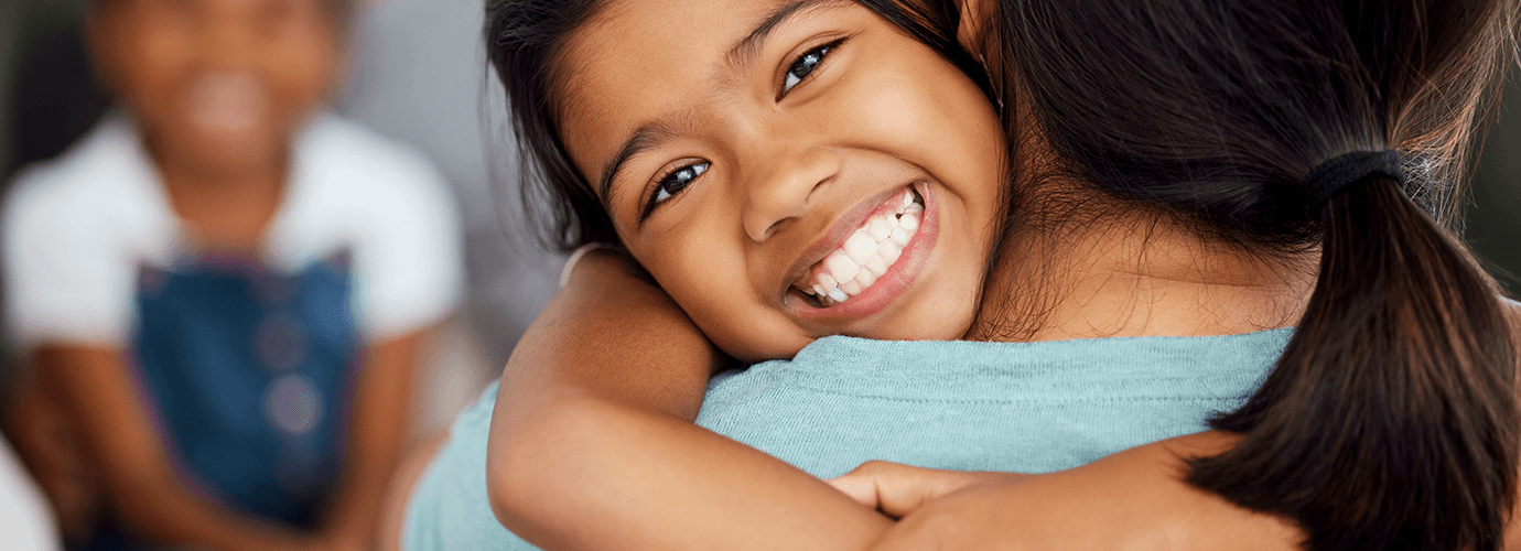A child hugging their parent with a big smile.