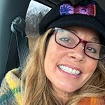 Courtney Winkler 150x150 Courtney is wearing glasses and a hat. She is smiling and wearing a colorful scarf.
