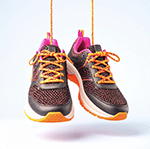 Pat Bernard 150x150 (1) A pair of running shoes are hanging by their laces. The shoes have bright orange and pink details, with charcoal grey uppers.